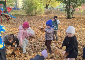 Grupa dzieci w ogrodzie przedszkolnym podrzuca do góry liście
