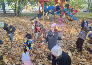 : Grupa dzieci w ogrodzie przedszkolnym podrzuca do góry liście