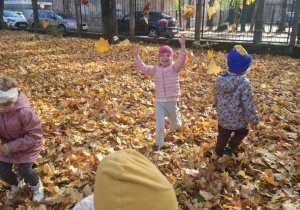 : Grupa dzieci w ogrodzie przedszkolnym podrzuca do góry liście