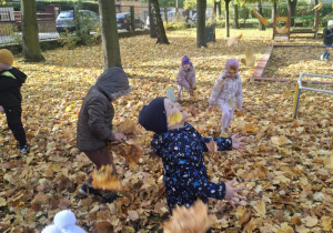 : Grupa dzieci w ogrodzie przedszkolnym podrzuca do góry liście