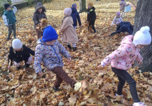 : Grupa dzieci w ogrodzie przedszkolnym podrzuca do góry liście