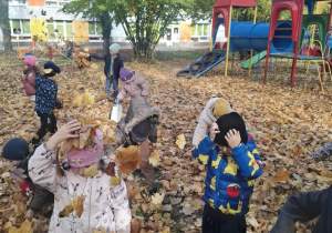 : Grupa dzieci w ogrodzie przedszkolnym podrzuca do góry liście