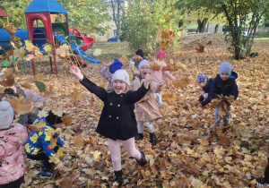 : Grupa dzieci w ogrodzie przedszkolnym podrzuca do góry liście