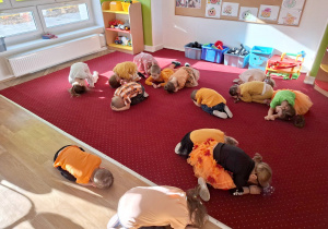 Dzieci leżą skulone na dywanie uczestnicząc w zabawie ruchowej