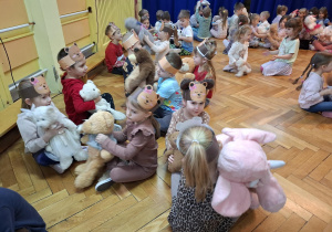 Dzieci siedzą w parach naprzeciwko siebie trzymając na kolanach pluszowe misie