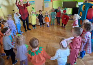 Dzieci wykonują pląsy do muzyki stojąc w kole w swoich grupach