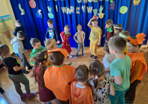 Dzieci wykonują pląsy do muzyki stojąc w kole w swoich grupach