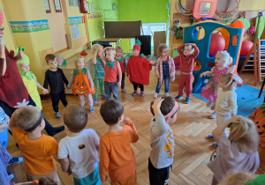 Dzieci wykonują pląsy do muzyki stojąc w kole w swoich grupach