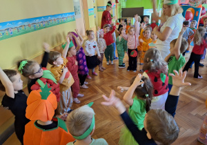 Dzieci wykonują pląsy do muzyki stojąc w kole w swoich grupach