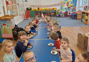 Dzieci siedzą przy stole i jedzą urodzinowe ciasto