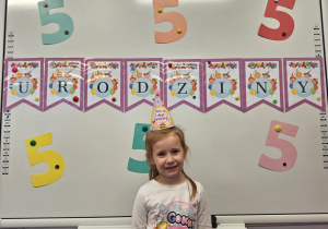 Dziewczynka stoi na tle urodzinowej dekoracji