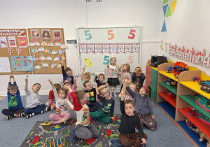 Dzieci siedzą na dywanie i trzymając w ręku lizaka pozują do zdjęcia z Laurą