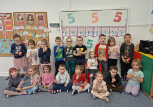 Cała grupa dzieci stoi na dywanie i pozuje do zdjęcia z Antosiem