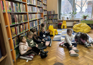 Dzieci siedzą przed regałem z ksiązkami