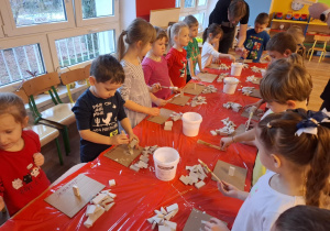 Dzieci stoją przy stole i sklejają gipsowe elementy choinki