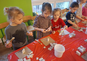 Dzieci stoją przy stole i sklejają gipsowe elementy choinki