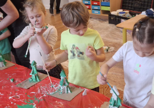 Dzieci stoją przy stole i malują zrobioną choinkę