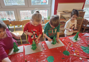 Dzieci stoją przy stole i malują zrobioną choinkę