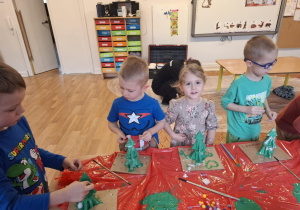 Dzieci stoją przy stole i malują zrobioną choinkę