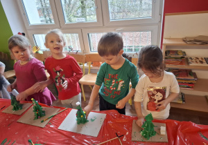 Dzieci stoją przy stole i malują zrobioną choinkę