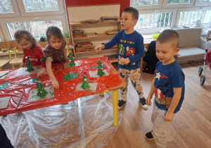 Dzieci stoją przy stole i malują zrobioną choinkę