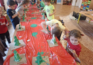 Dzieci stoją przy stole i malują zrobioną choinkę