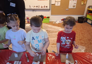 Dzieci stoją przy stole i sklejają gipsowe elementy choinki