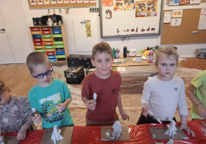 Dzieci stoją przy stole i sklejają gipsowe elementy choinki