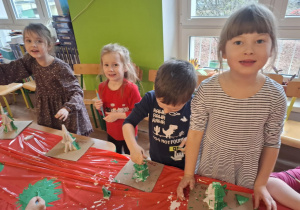 Grupa dzieci stoi przy stole i maluje zrobioną choinkę