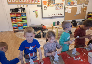 Dzieci stoją przy stole i sklejają gipsowe elementy choinki