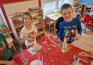 Dzieci stoją przy stole i sklejają gipsowe elementy choinki