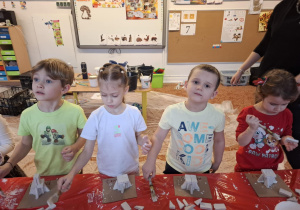 Dzieci stoją przy stole i sklejają gipsowe elementy choinki