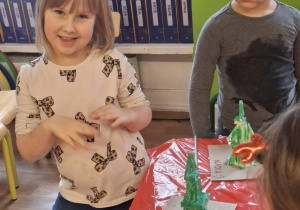 Dziewczynki stoją przy stole i malują zrobioną choinkę