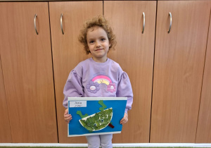 Dziecko pozuje do zdjęcia trzymając logo grupy przygotowane przez rodziców