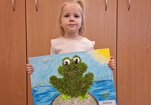 Dziecko pozuje do zdjęcia trzymając logo grupy przygotowane przez rodziców