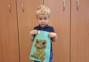 Dziecko pozuje do zdjęcia trzymając logo grupy przygotowane przez rodziców