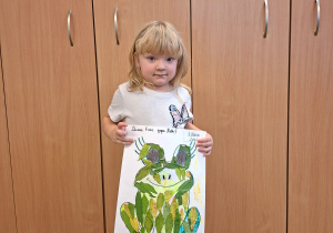 Dziecko pozuje do zdjęcia trzymając logo grupy przygotowane przez rodziców