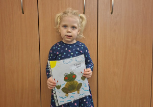 Dziecko pozuje do zdjęcia trzymając logo grupy przygotowane przez rodziców