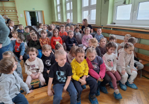 Dzieci siedzą na ławkach i oglądają jasełka