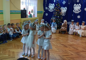 Dziewczynki w przebraniu śnieżynek stoją na środku sali i recytują wiersz