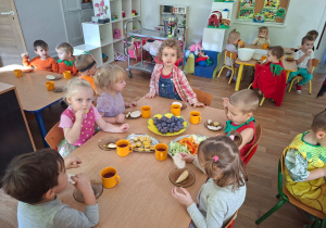 Dzieci przebrane za owoce i warzywa siedzą przy stole i jedzą zdrowe owoce i warzywa