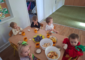 Dzieci przebrane za owoce i warzywa siedzą przy stole i jedzą zdrowe owoce i warzywa