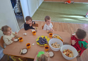 Dzieci przebrane za owoce i warzywa siedzą przy stole i jedzą zdrowe owoce i warzywa