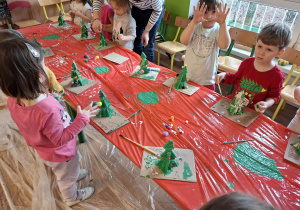 Dzieci ozdabiają kolorowymi pomponami wykonane przez siebie choinki
