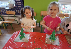 Dwie dziewczynki ozdabiają kolorowymi pomponami wykonane przez siebie choinki