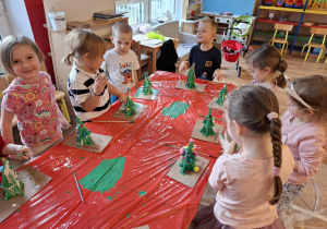 Dzieci ozdabiają kolorowymi pomponami wykonane przez siebie choinki