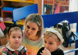 Dwie dziewczynki siedzą przy stole razem z rodzicem