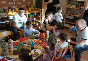 Dzieci wspólnie z rodzicami jedzą słodki poczęstunek