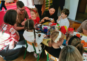 Dzieci wspólnie z rodzicami jedzą słodki poczęstunek