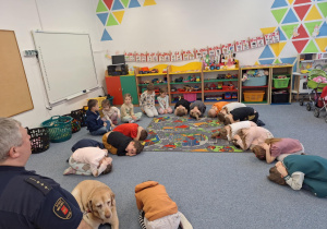 Dzieci na dywanie pokazują pozycję jaką należy przyjąć przy ataku psa